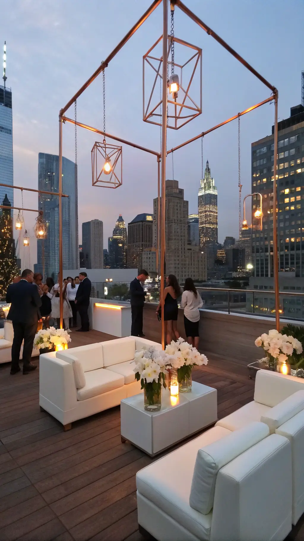 Magical May Wedding Ideas: A Spring Celebration Guide A stylish rooftop cocktail hour at blue hour with white leather furniture, lucite tables, and suspended copper frames adorned with white orchids, overlooking a twinkling city skyline.