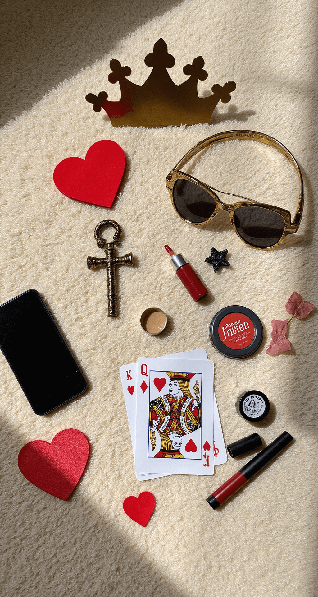 The Ultimate Queen of Hearts Halloween Costume A budget-friendly flat lay on a plush cream carpet features DIY Queen of Hearts accessories, including a handcrafted paper crown, a painted dollar store scepter, playing card details, and drugstore red and black makeup essentials, all illuminated by mid-morning sunlight. An iPhone and craft supplies hint at the accessible creation process, captured in an overhead shot that emphasizes the creative arrangement.