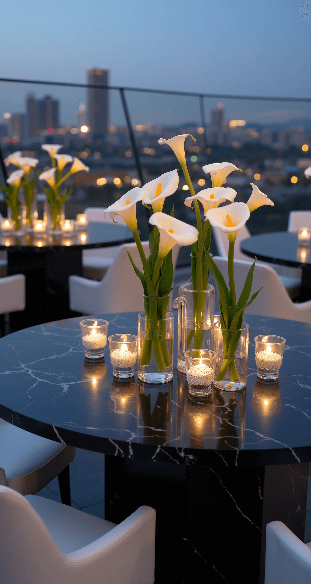 White Wedding Centerpieces: A Complete to Timeless Elegance Modern rooftop venue at twilight featuring minimalist white calla lily arrangements in tall geometric vases atop black marble tables, with city lights twinkling in the background and uplighting enhancing each centerpiece, complemented by white leather seating and chrome accents, captured from an elevated angle.