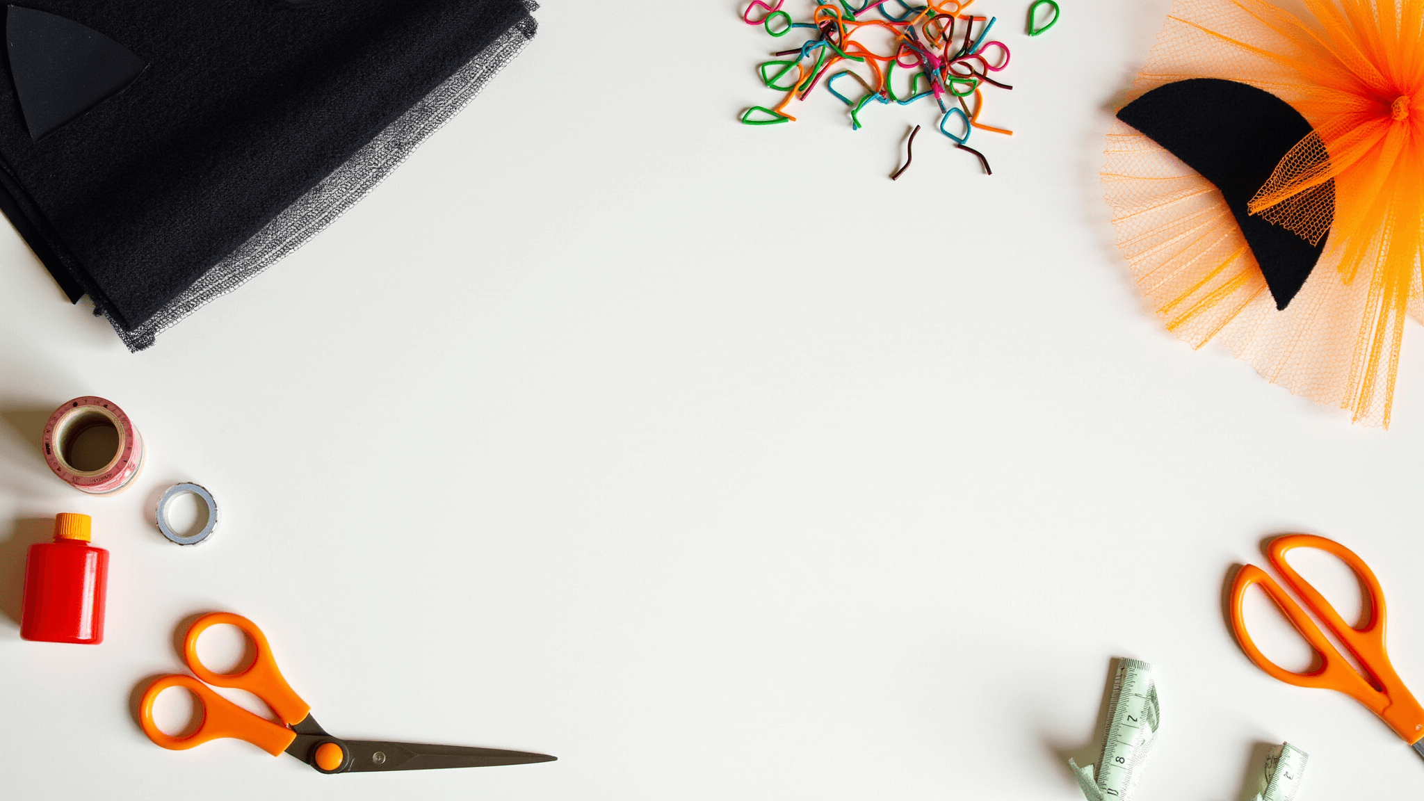 Bright overhead view of a minimalist craft workspace featuring Halloween cat costume materials like black fabric, felt cat ears, colorful pipe cleaners, and tulle, with neatly arranged creative tools and warm orange accents under natural lighting.