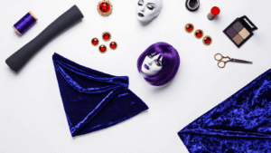 Creating a Raven Teen Titans Cosplay (That Actually Looks Amazing!) Overhead flatlay of Teen Titans Raven cosplay components on a white background, featuring a dark purple bodysuit, blue velvet cape, red gems, gray makeup, a purple wig, and sewing supplies, all illuminated with studio lighting.